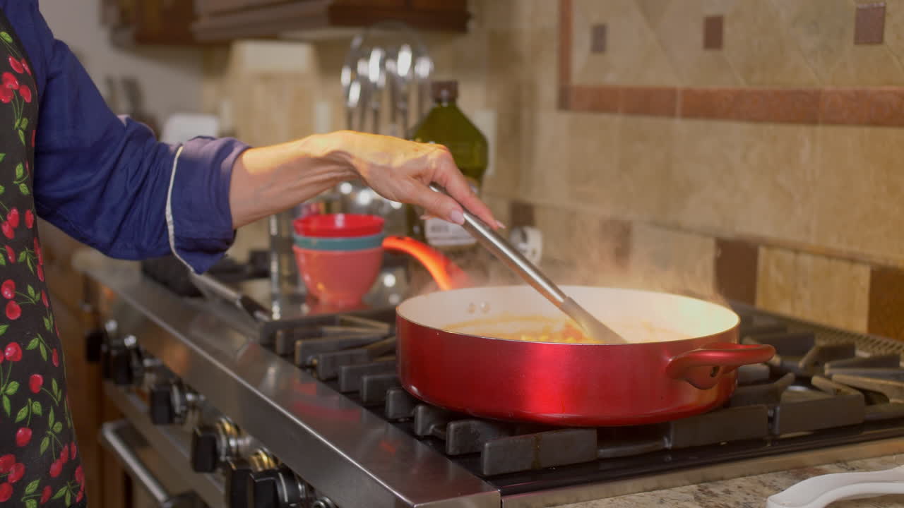 mujer cocinando comida en una sartén roja y agitándola con una cuchara en cámara lenta
