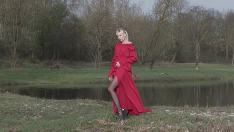 a model posing in a nature with vibrant red dress alone