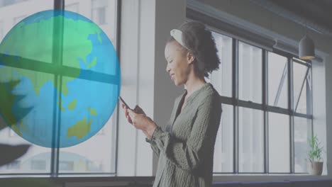 animation of globe over african american businesswoman using smartphone at office