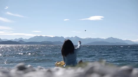 맑은 날에 해안선에 앉아 nahuel huapi 호수에 돌을 던지는 여자