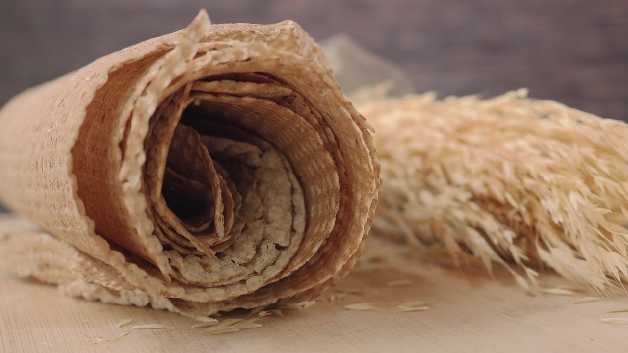 Pane piatto integrale arrotolato con spighe di grano essiccate.