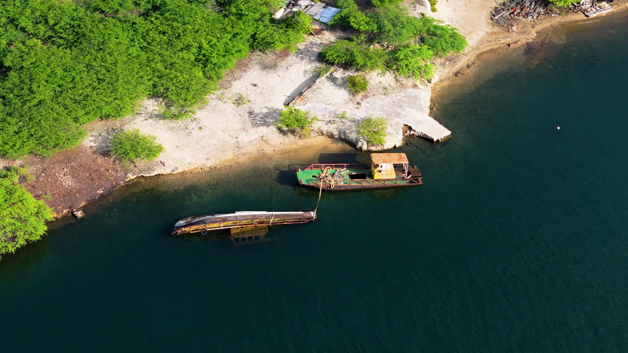 un avión no tripulado orbita alrededor de un barco hundido o abandonado anclado en una playa costera de arena blanca.