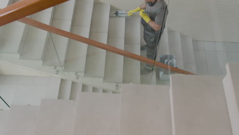 vista superior de un limpiador árabe con guantes limpiando escaleras con un trapeador dentro de un edificio de oficinas 1