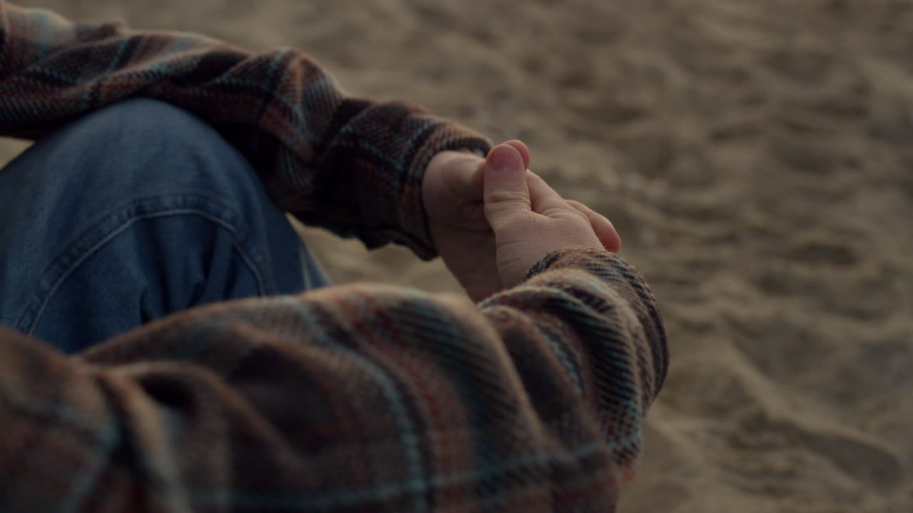 모래 해변에 혼자 앉아 있는 알아볼 수 없는 남자. 클로즈업 남자 손을 잡고