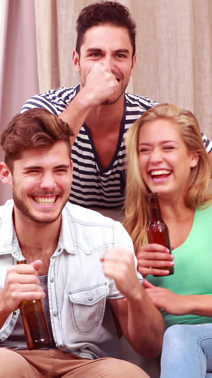 Amici sorridenti che guardano la TV mentre mangiano popcorn e bevono birra