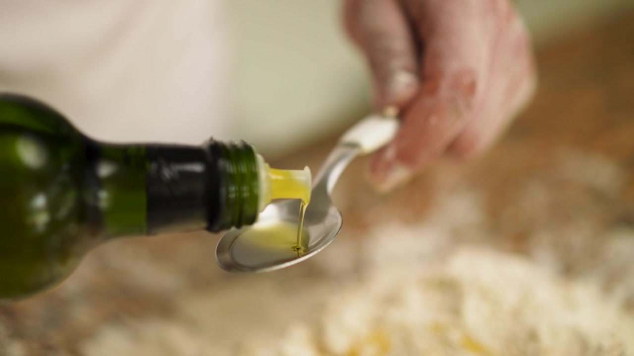 L'intricato processo di preparazione dell'impasto ripreso mentre uno chef aggiunge olio d'oliva alla farina su un piano di lavoro