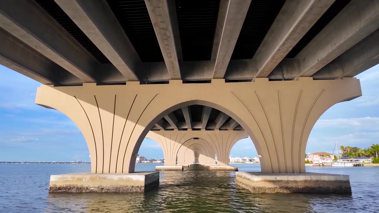 A boat cruises beneath the Pinellas Bayway Bridge near Pass-a-Grille, revealing the famous "Cathedral Under the Bridge" perspective created by its soaring arches and reflections.