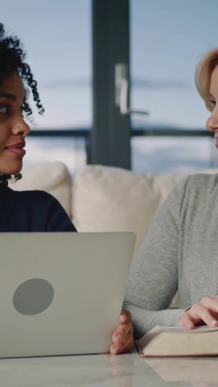 Video verticale: Donna a sinistra che controlla il laptop, guarda a destra e la esorta a voltarsi sul divano con un libro.