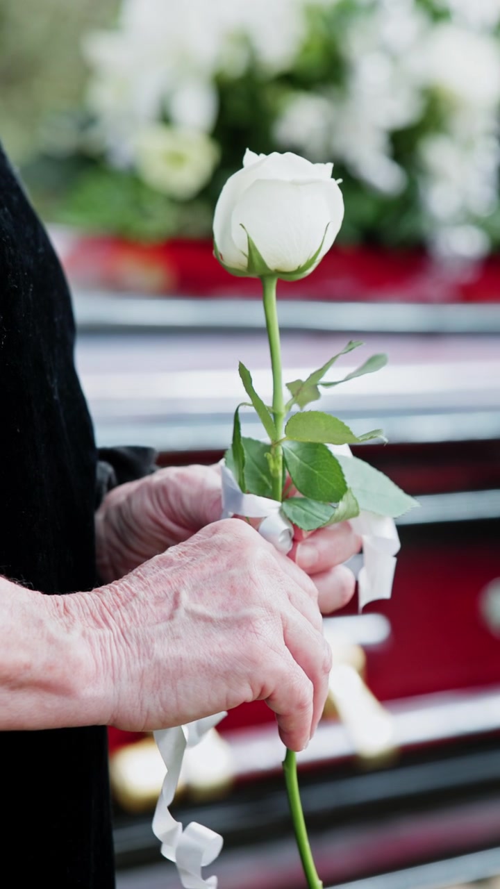 Persona anziana che tiene una rosa bianca a un funerale