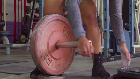 female weight lifter adding weights to her lifting bar at the gym