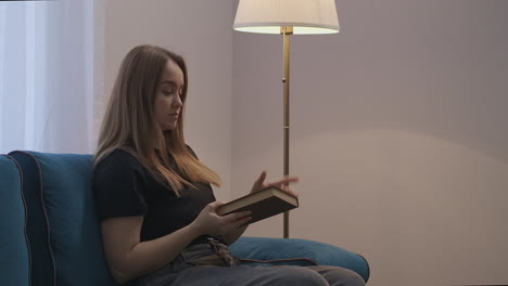 pretty-student-woman-is-reading-book-at-home-at-evening-and-switching-on-floor-lamp-rest-and-relax-at-weekend-interior-of-living-room