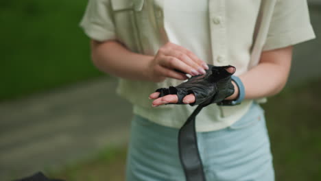 close-up of woman wearing black gloves with focus on hands and smartwatch on right wrist, surrounded by blurred green scenery and outdoor path hints