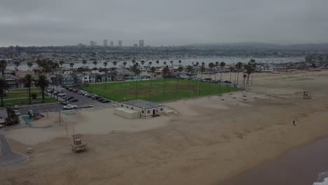 Bewölkter-Morgenstrand-An-Der-Westküste-Mit-Grünem-Park-Und-Aufsteigenden-Palmen,-Blick-Auf-Den-Yachthafen-Und-Die-Stadt