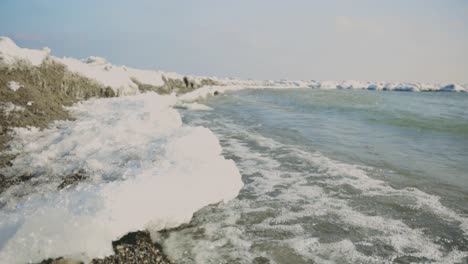 movimiento de olas salpicando pequeñas estructuras de hielo a lo largo de la costa - ángulo bajo, primer plano