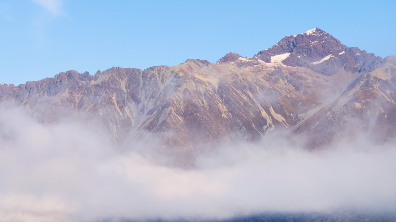 Mountain peaks partially obscured by rolling fog under a clear blue sky. Captured in Glenorchy, New Zealand