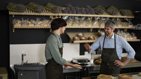 Smiling-young-cashier-giving-paper-bag-to-the-female-customer.-Woman-leaves-with-smile-on-her-face.-Happy-Father-and-son-high