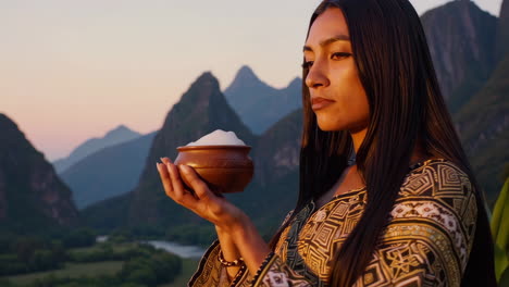 woman in traditional attire holds a bowl at sunset