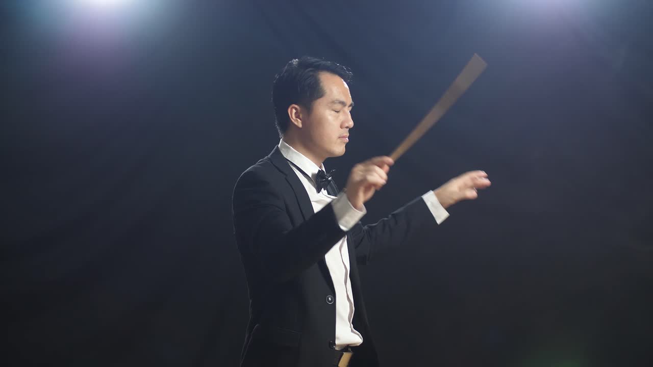 흑인 스튜디오에서 눈을 감고 몸짓을 하는 아시아계 지휘자 남자.