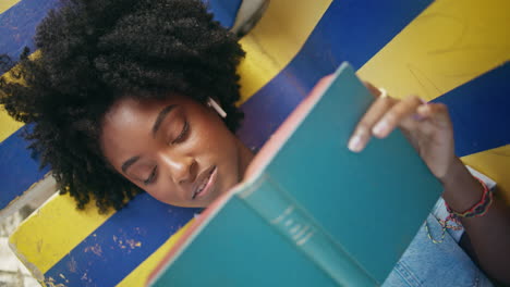 portrait girl holding book lying on bench outdoors. female student reading novel