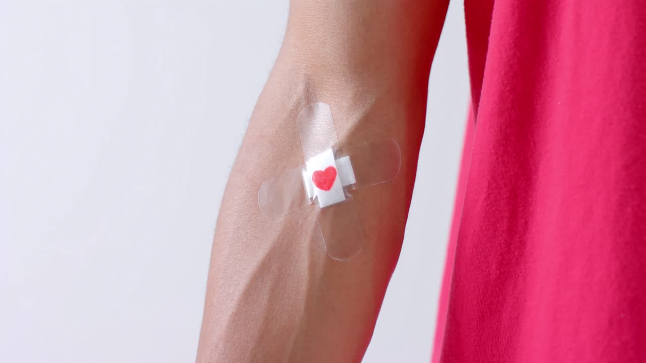 primer plano del brazo de un hombre biracial con un corazón pegando yeso en el brazo, sobre un fondo blanco, cámara lenta