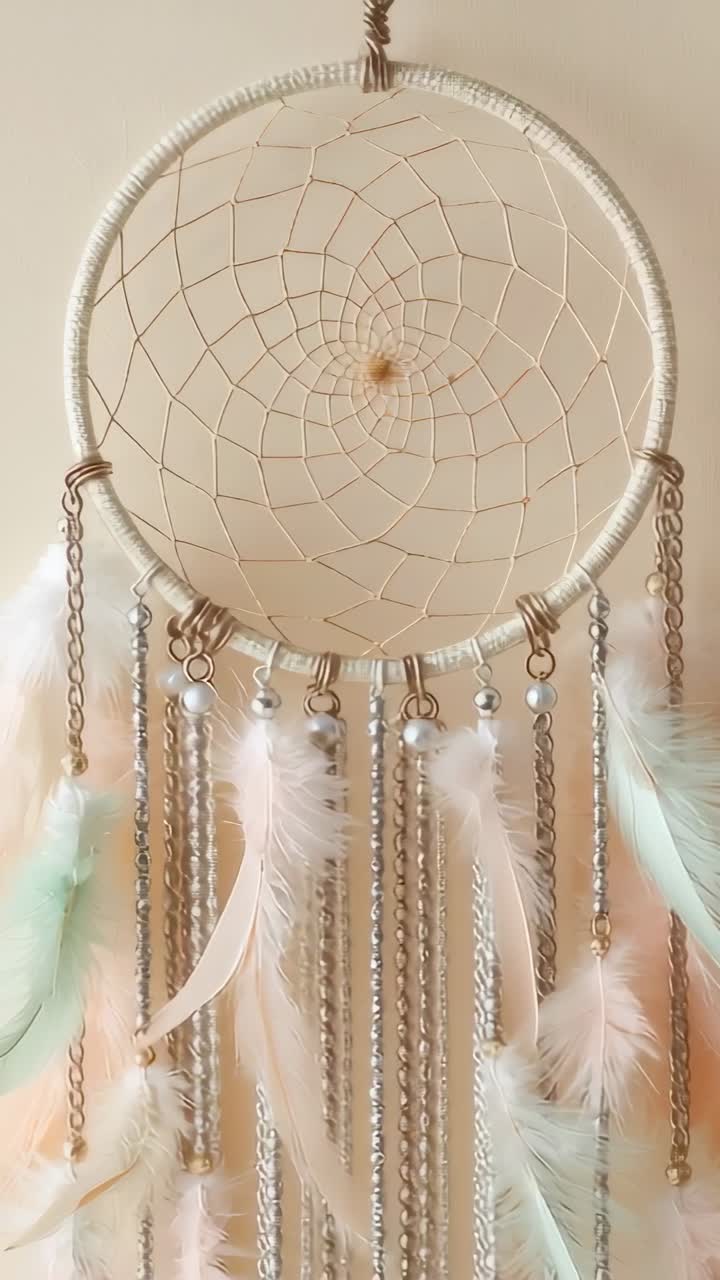Vertical video: Breeze initiating dreamcatcher swaying against beige wall, with beads and feathers