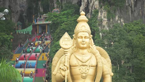 (selective focus) stunning view of the lord murugan statue in the foreground and tourists climbing a colorful stairs leading to the batu caves in the background. kuala lumpur, malaysia