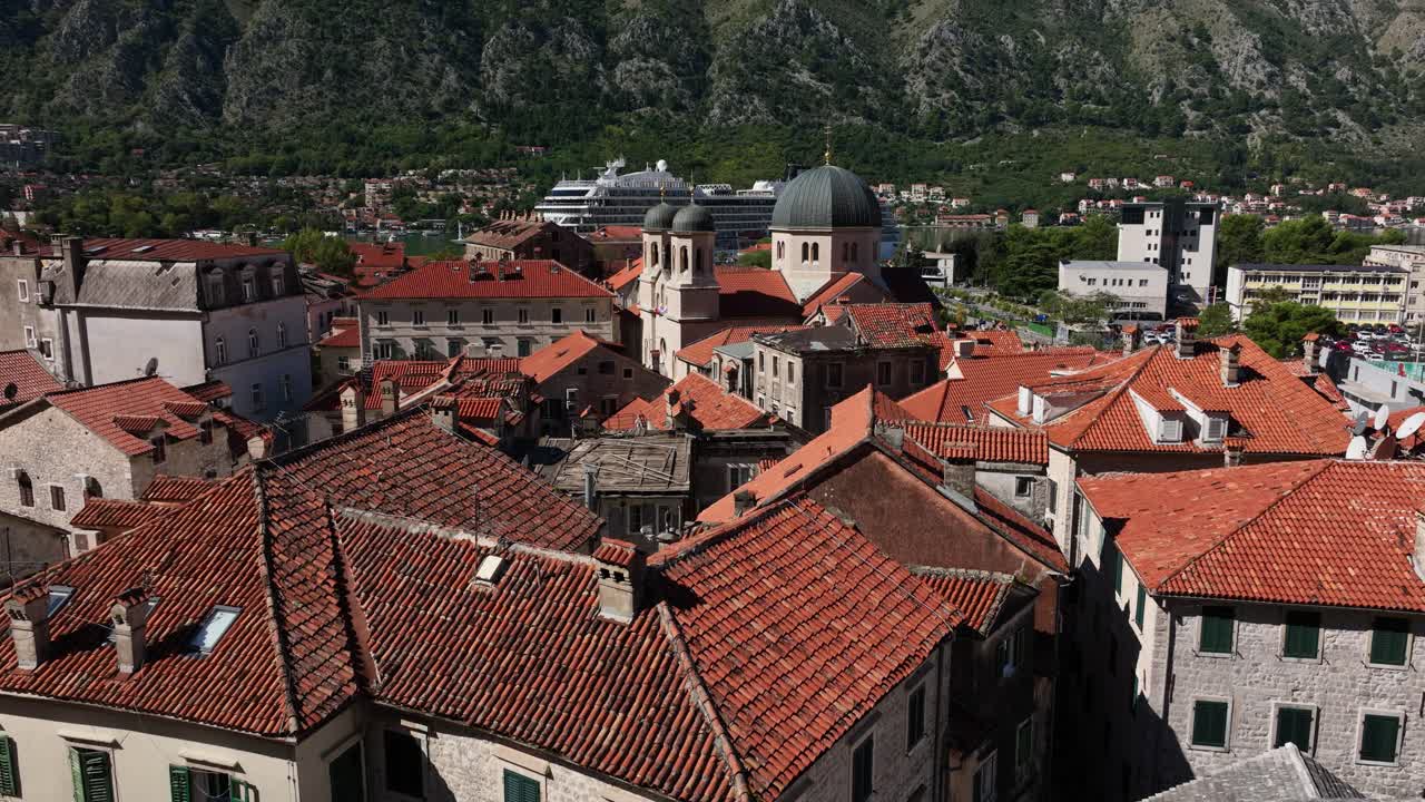 Red rooftops of Kotor old town with mountains and cruise ship in background, sunny day