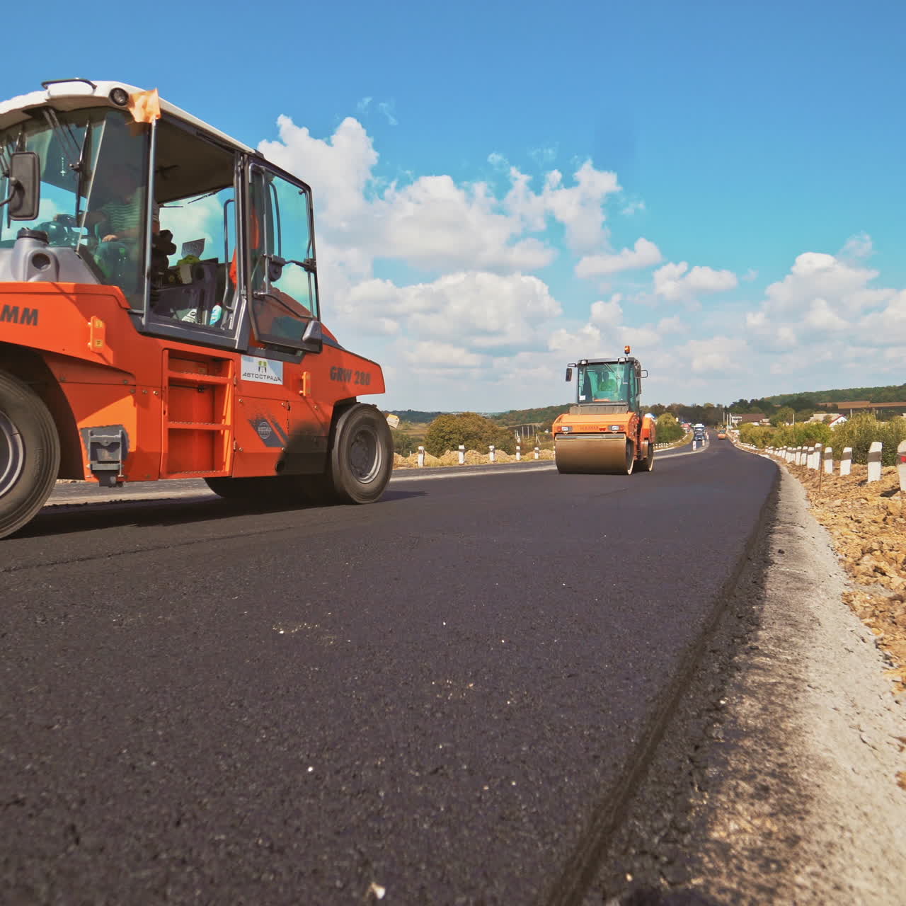 workers carry out construction and repair works of roads with the help of professional equipment near the city in the summer. Close-up