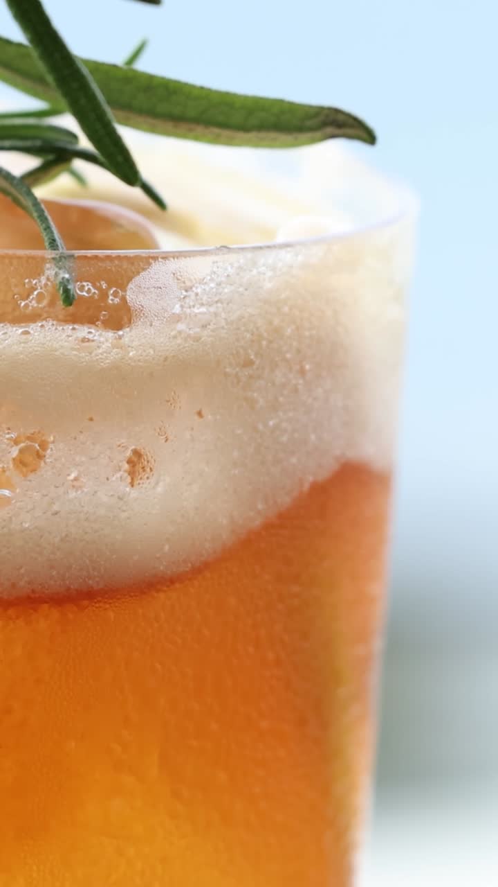 Primo piano di un vivace cocktail agli agrumi guarnito con erbe fresche, che mostra condensa e ghiaccio in un ambiente luminoso.