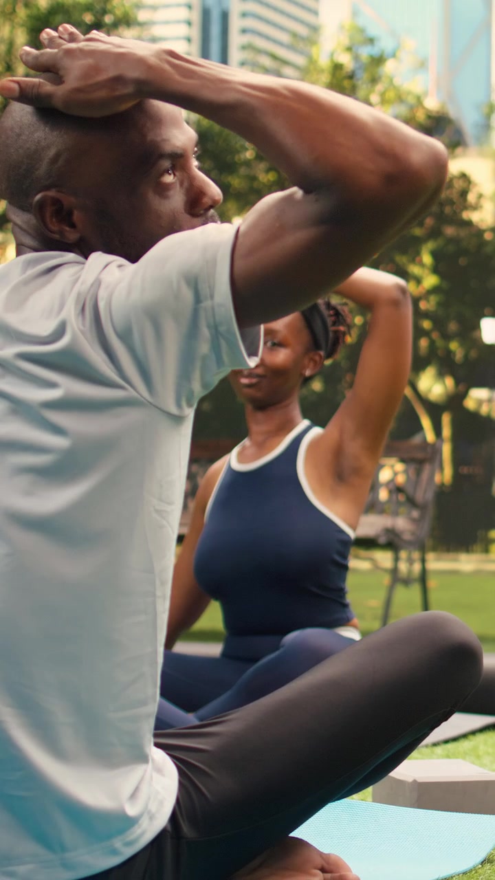 Video verticale Istruttore di yoga di fronte ai partecipanti seduti a gambe incrociate sui tappetini in un parco cittadino