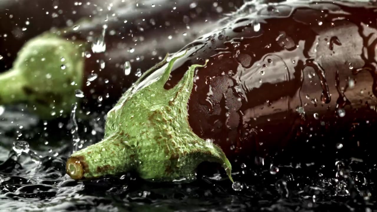 Närbild på färsk aubergine med vattenstänk i slow motion