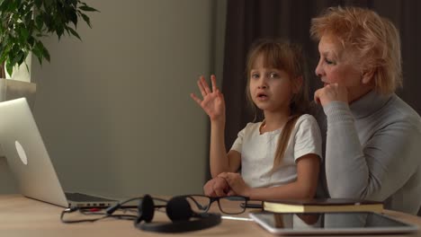 Beginning-of-online-school-classes,-greeting-the-teacher-using-a-video-call.-A-young-grandmother-and-granddaughter-study-on-a-laptop