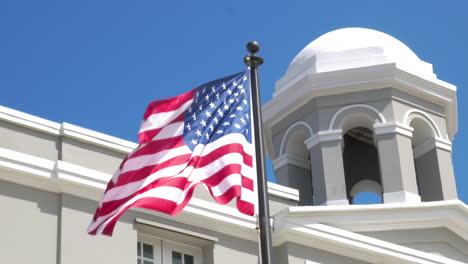 An-American-flag-waving-in-the-wind-in-front-of-a-white-historic-building-in-Old-San-Juan,-Puerto-Rico