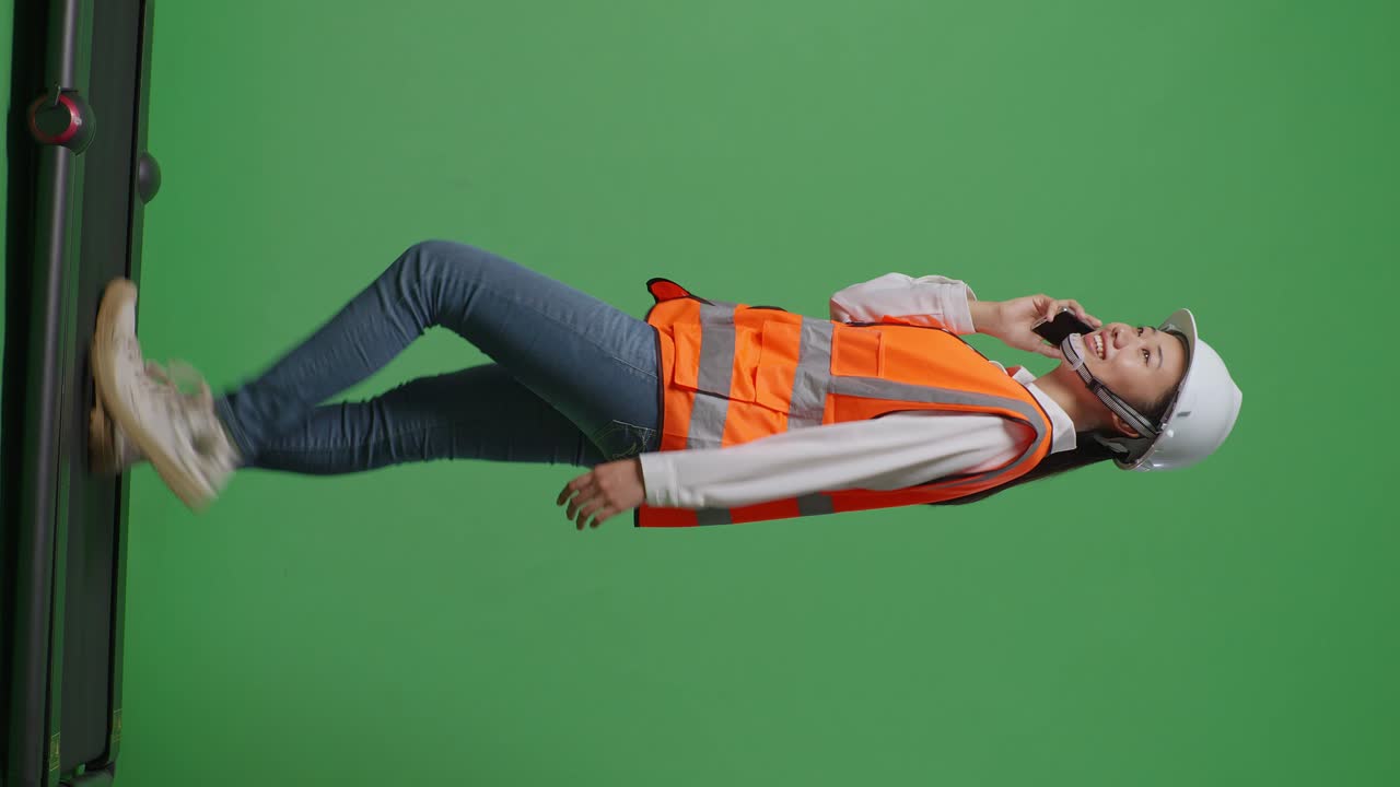 안전 헬을 입은 아시아 여성 엔지니어가 녹색 스크린을 배경으로 는 동안 스마트폰으로 이야기하는 측면 뷰