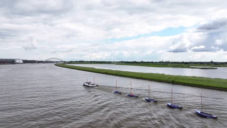 A-Motorboat-Towing-a-Line-of-Six-Small-Boats-on-the-Noord-River-in-Hendrik-Ido-Ambacht,-South-Holland,-Netherlands---Aerial-Drone-Shot