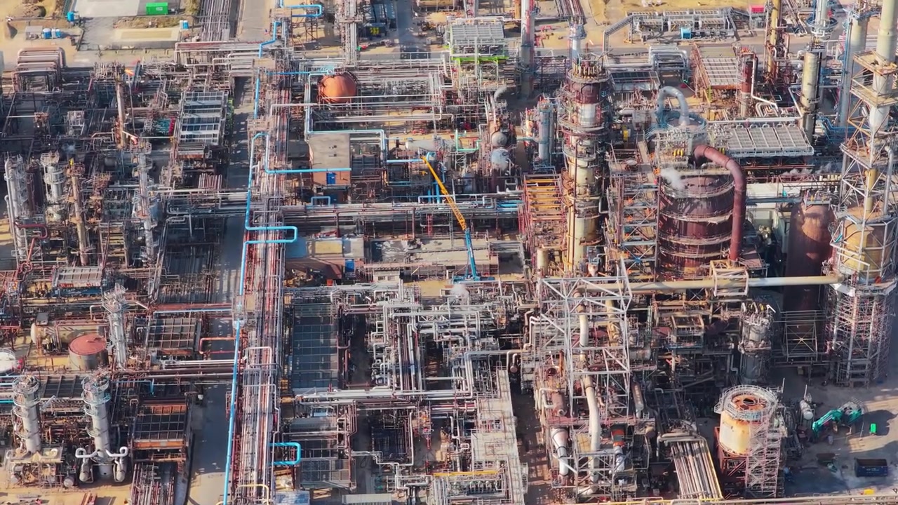 High angle perspective of an expansive oil refinery with metal structures pipes and tanks operating during the day under bright sunlight in an industrial zone