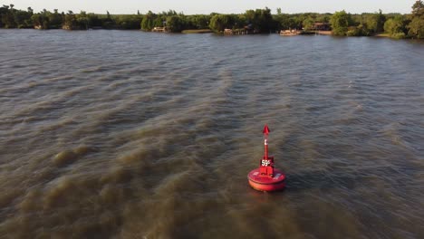 Tiro-Hacia-Atrás-De-Una-Boya-Roja-Flotando-En-El-Agua-Marrón-Del-Río-Paraná,-Hidrovi-A-En-Argentina