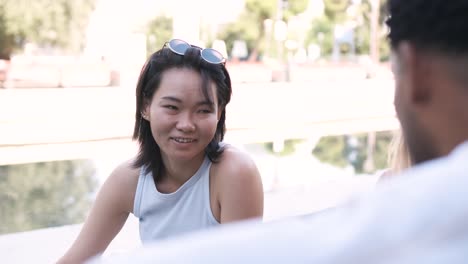 happy woman listening to man talking at city park during sunny day