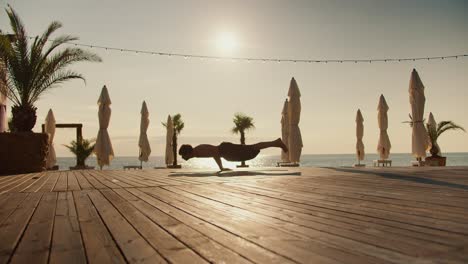 The-yogi-guy-keeps-his-body-on-weight,-remaining-on-two-hands.-Yoga-practice-and-zen-stall-on-sunny-beach