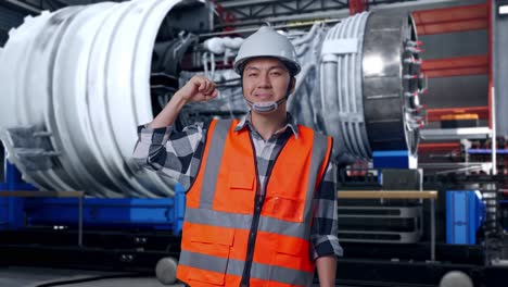 asian male engineer with safety helmet flexing his bicep and smiling to camera while standing with airplane engine maintenance conducted, analytics checking the turbine