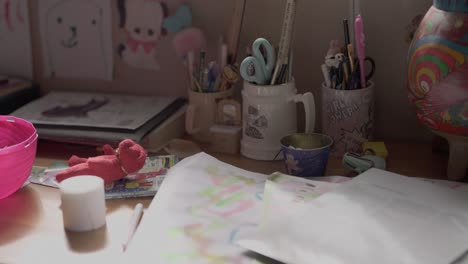 a child's artwork is spread over a table. jars filled with pencils, pens, scissors and other craft items are on the table.