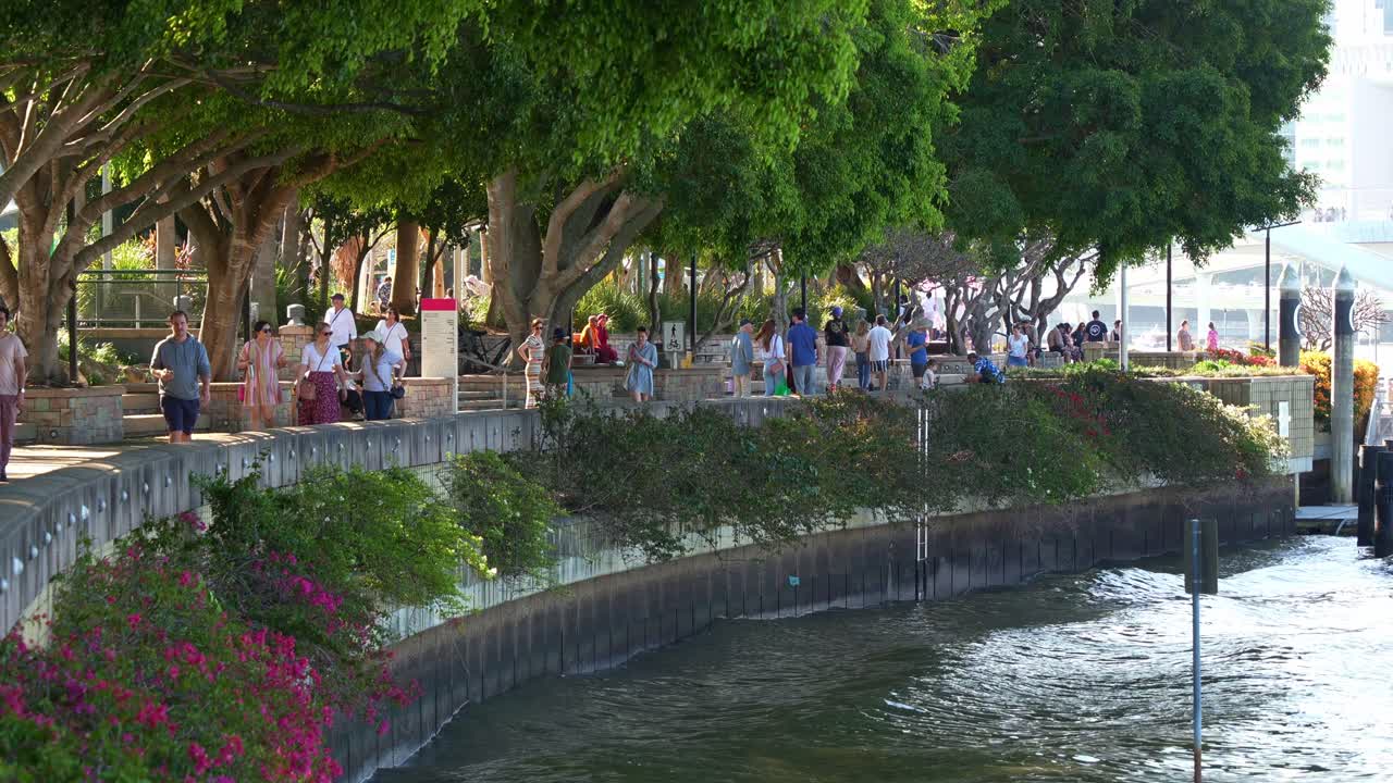 Slow motion shot of people walking and strolling along the riverside Clem Jones Promenade in South bank on the weekend, a tranquil oasis of Brisbane lifestyle recreational precinct by the river.