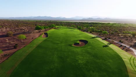 push-in drone shot of a desert golf fairway with visible cart tracks, bunkers, and mountain views at sunrise