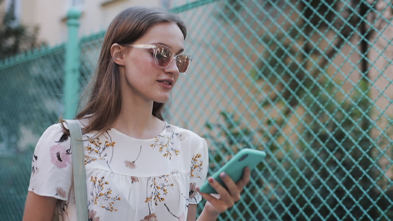 Giovane donna con occhiali da sole che controlla il suo smartphone all'aperto