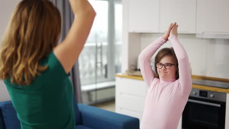 niña con síndrome de down y su madre practicando yoga en casa, posición de árbol