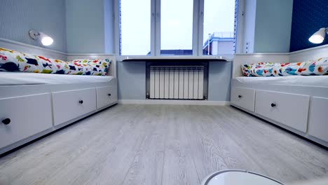 a robotic vacuum moves along wooden planks in childrens bedroom.