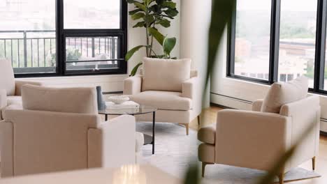 four-white-chairs-in-a-seating-area-or-living-room-of-a-home-next-to-windows-letting-in-natural-sunlight