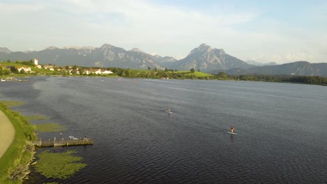 aerial view of people using stand up paddle boards on lake in bavaria, mountains in background