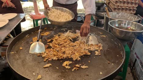 cooking noodles on a large outdoor griddle.