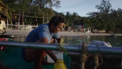 man scooping water from a boat near a tropical beach